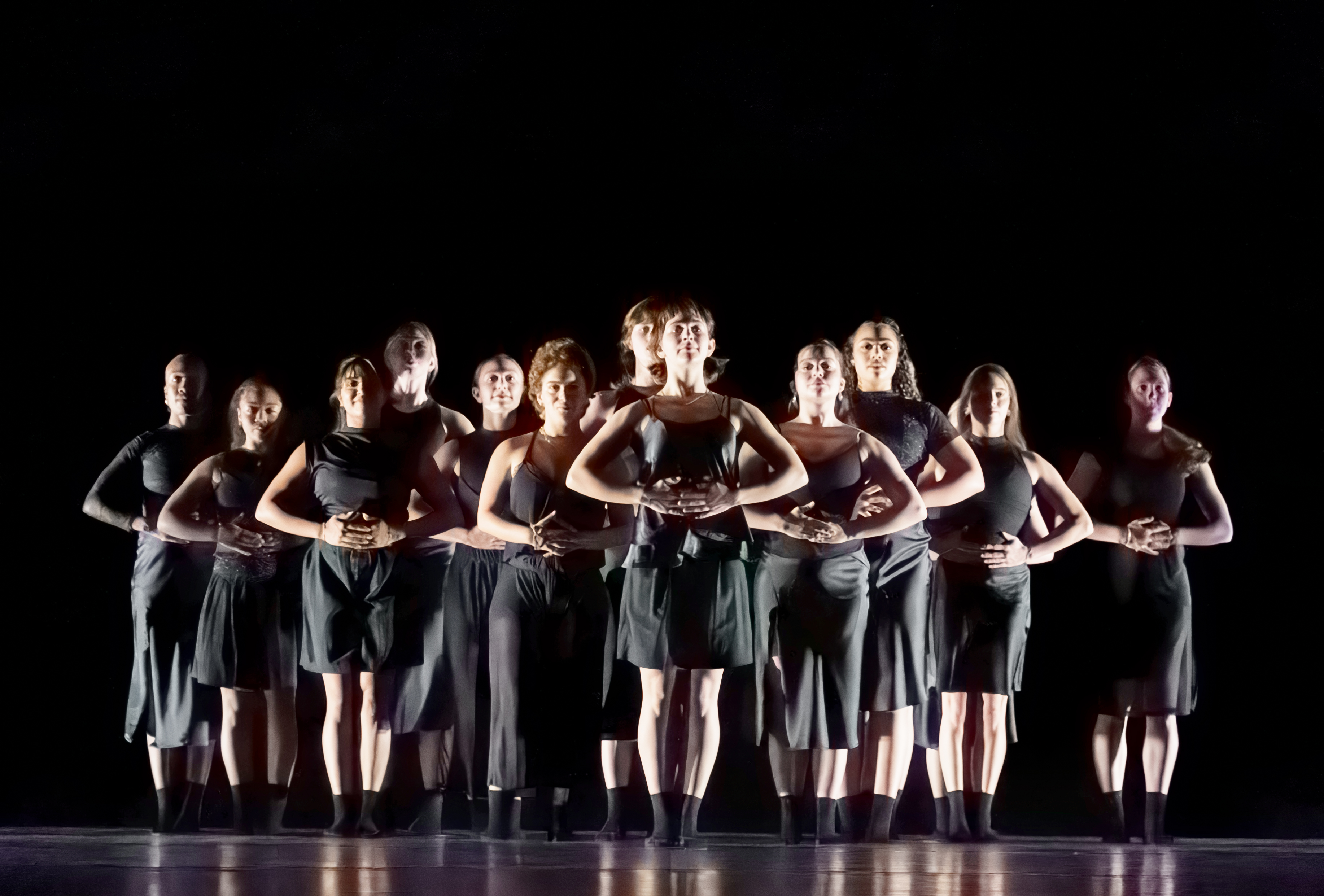 group of dancers against in all black against black background