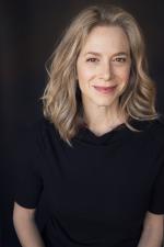 Headshot photo of white woman with light hair wearing a black shirt against a black background